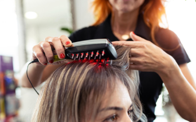 Hair stylist uses a red LED light comb on a client's scalp during a hair treatment at a salon.