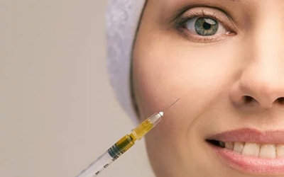 Close-up of a smiling woman as a syringe is poised near her cheek for a cosmetic facial injection.