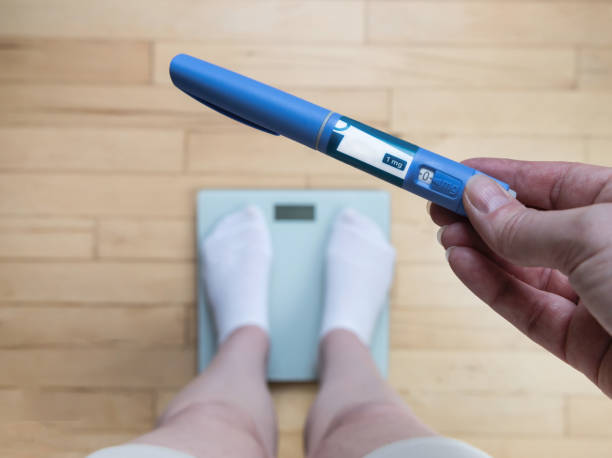 Hand holding a blue digital pregnancy test above a bathroom scale as a person stands on the scale.