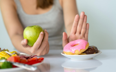 â___Reduced cravings Person holding a green apple while signaling to resist two donuts on a plate.