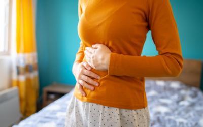 â___Slowed gastric emptying Person in an orange top clutching their abdomen, suggesting stomach pain or abdominal discomfort in a bedroom setting.