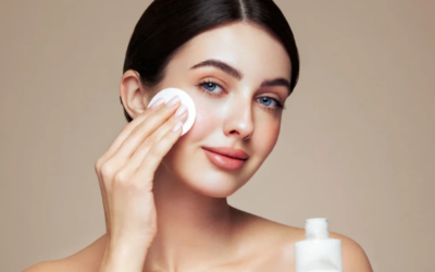 â_¢ Step 8_ Home care plan Woman gently wiping her cheek with a cotton pad during a skincare routine, with a bottle of product nearby on a neutral background.