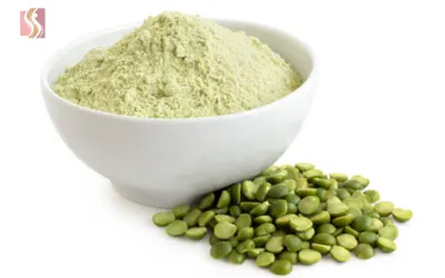 White bowl filled with pale green pistachio powder, with shelled pistachio nuts arranged beside it.