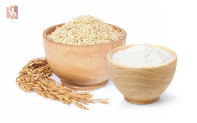 Two wooden bowls—one with cooked rice and the other with yogurt—set beside rice stalks.