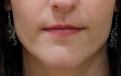 Close-up of a woman's mouth and chin, with neutral lipstick and decorative earrings.