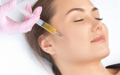 â___Exosome Therapy for Pigmentation Support Close-up of a clinician injecting a cosmetic syringe into a woman's cheek as she rests with her eyes closed.